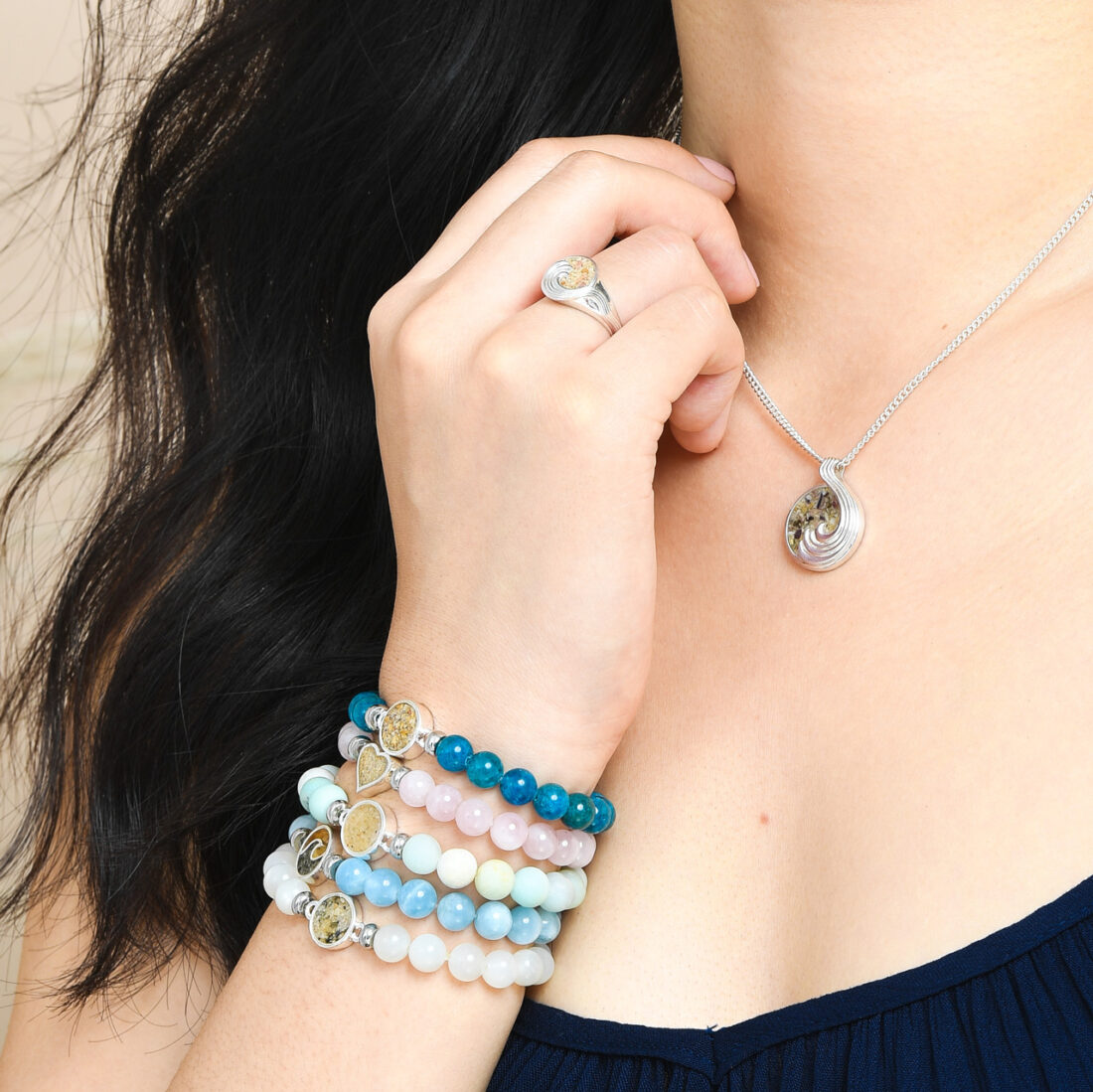 Close-up of hand wearing stacks of beaded bracelets with healing crystals and sand and earth elements. Perfect Valentine's Day jewelry gift.