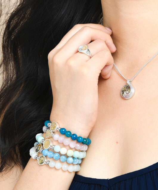 Close-up of hand wearing stacks of beaded bracelets with healing crystals and sand and earth elements. Perfect Valentine's Day jewelry gift.