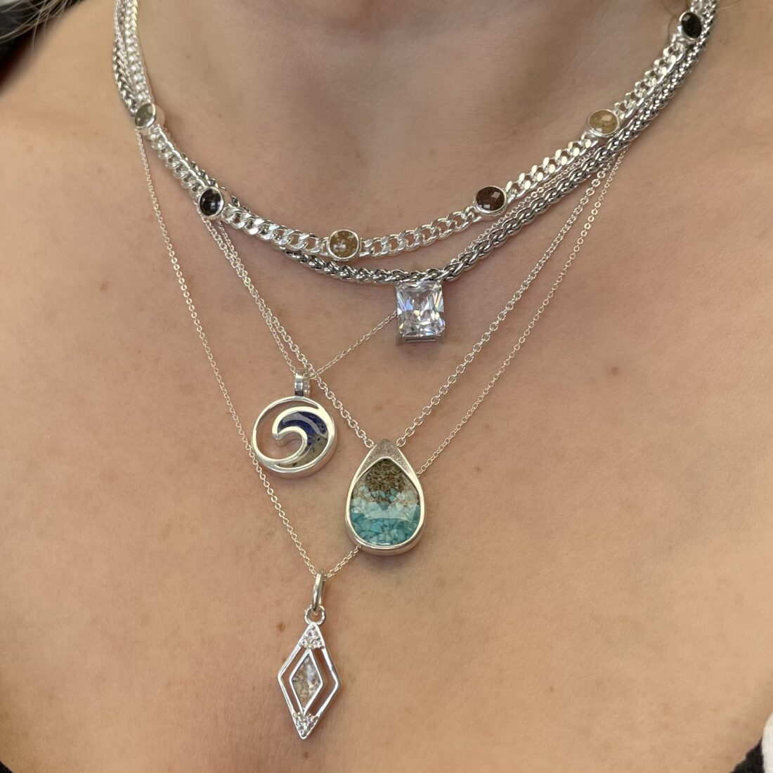 Sterling silver necklaces, including the World Traveler Necklace, layered on neck, close-up shot.