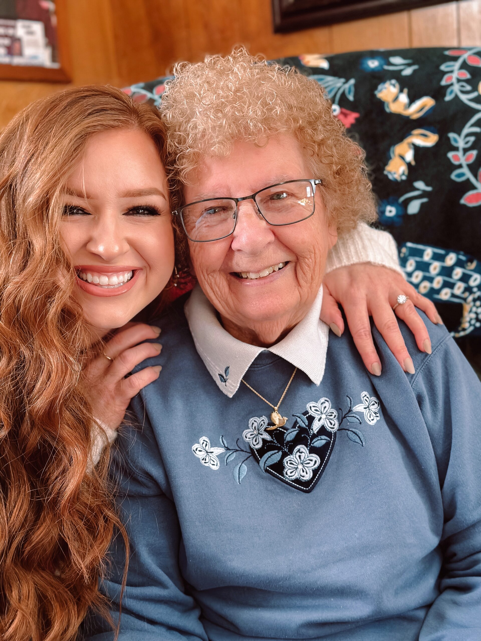 The author, Jami, and her grandmother both look into camera smiling as her grandmother wears her new gold cardinal necklace with beach sand.