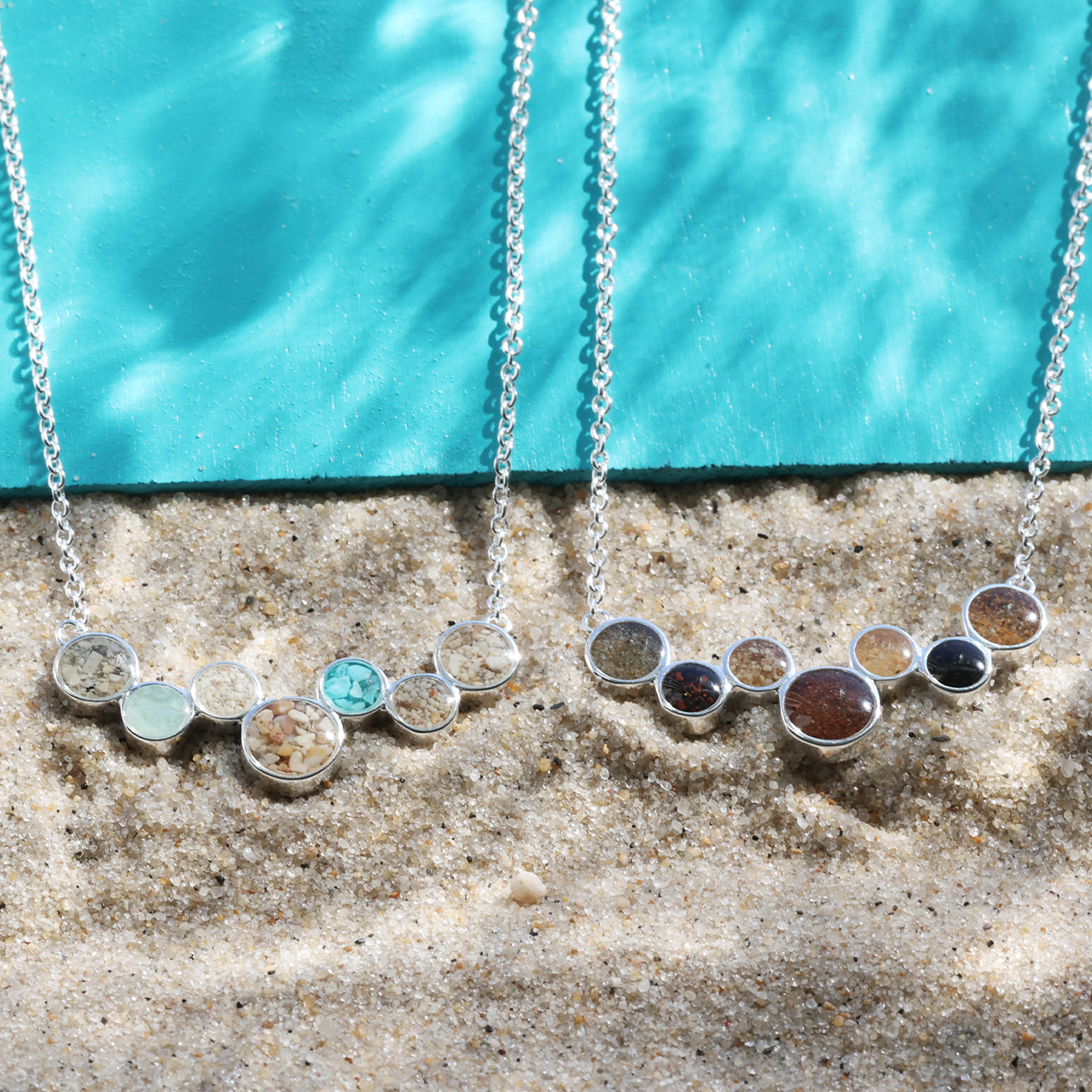 Product shot of two The World Is Yours Stationary Necklaces with sand from all 7 continents.