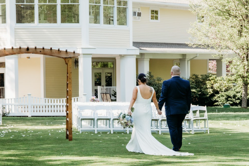 Bride and groom holding hands in lawn walking away from camera.